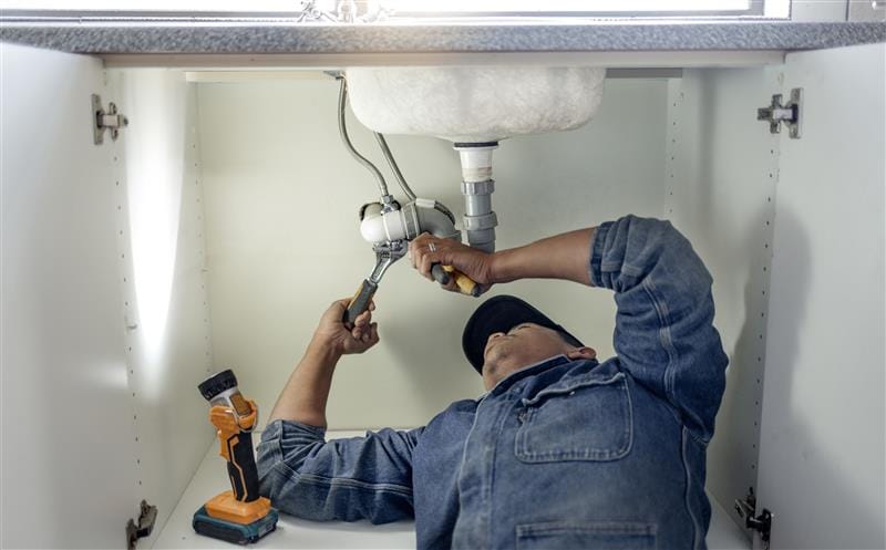 Plumber repairing pipes beneath a bathroom sink in Selma
